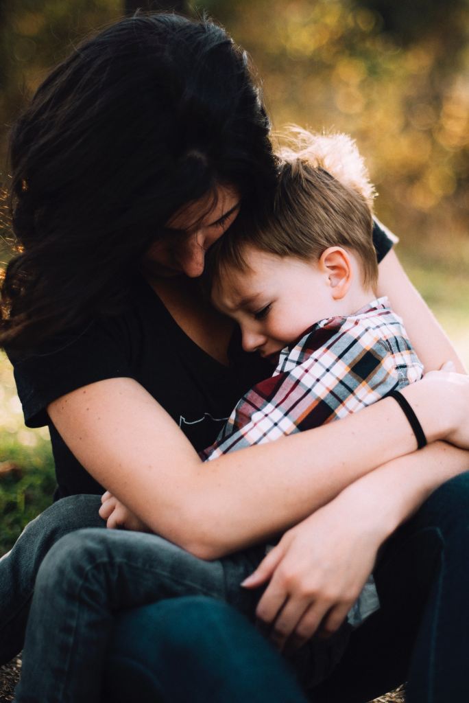 Mother comforting small boy. Image by Jordan Whitt on Unsplash.